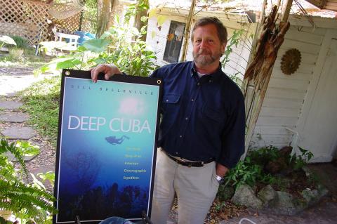 Author Bill Belleville stands in his backyard with a poster for the release of one his many books, ‘Deep Cuba.’ 